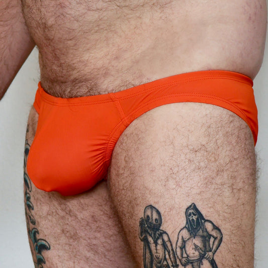 Person wearing bright orange men's underwear with tattoos on legs.