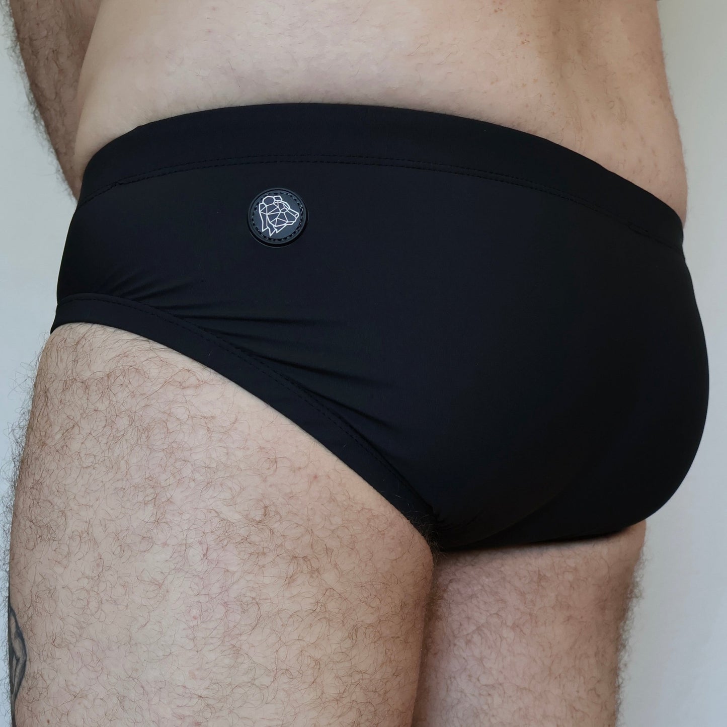 Black swim briefs worn by a person on a plain background