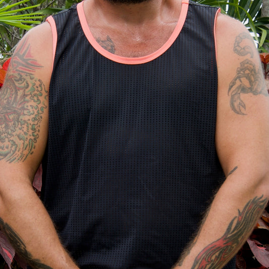 Person wearing a black tank top with pink trim, sitting outdoors with greenery in the background.