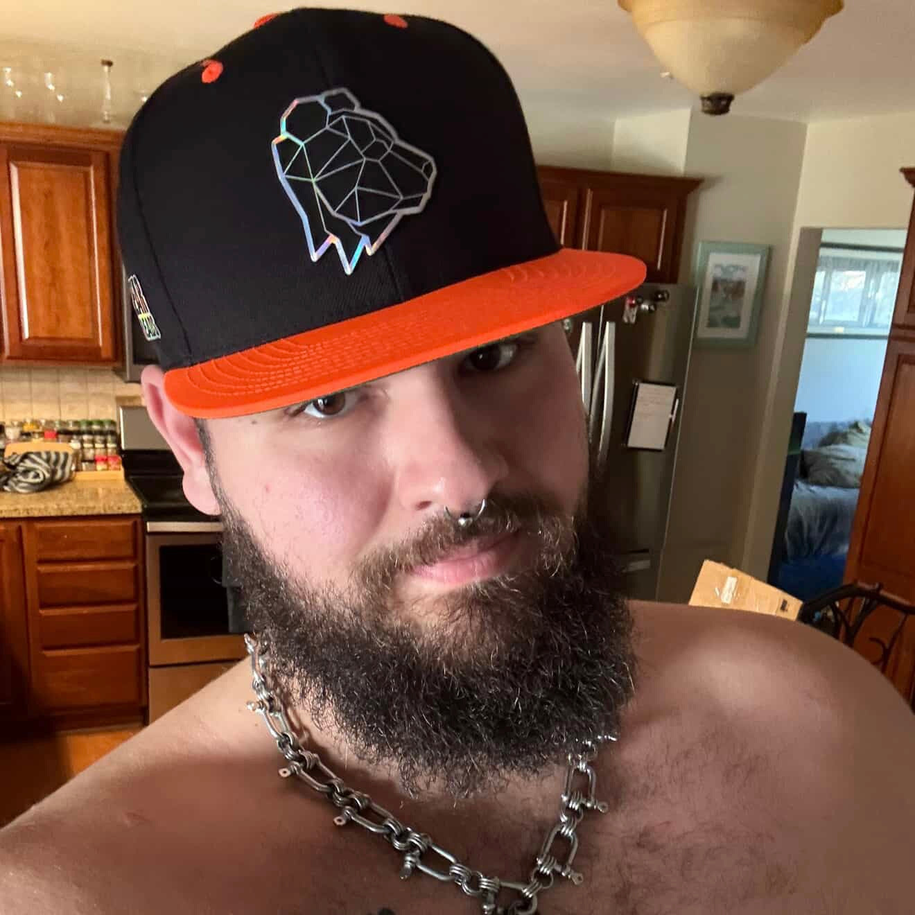 Man wearing a black and orange cap with a geometric design in a kitchen.
