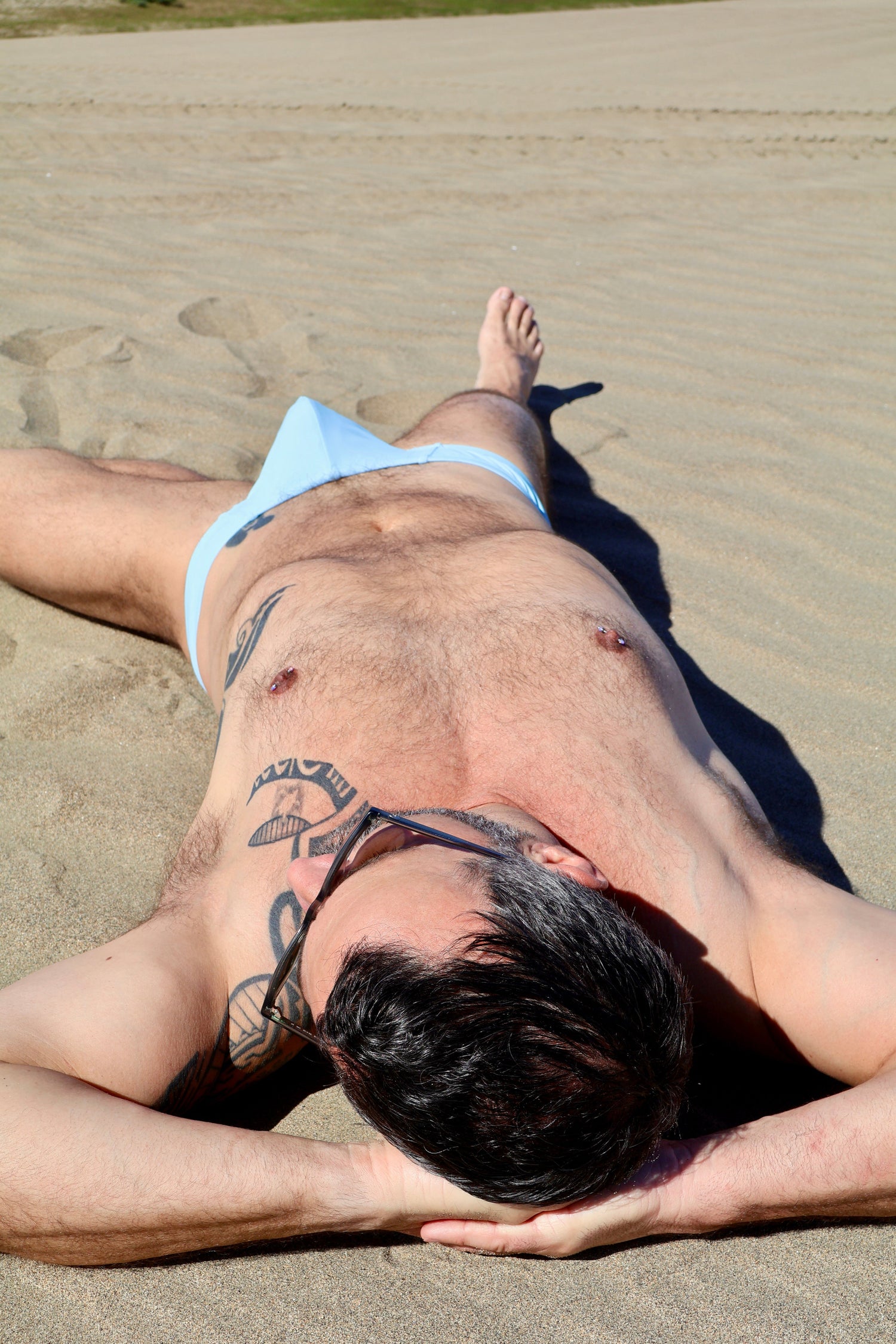 Person lying on the sand with tattoos visible