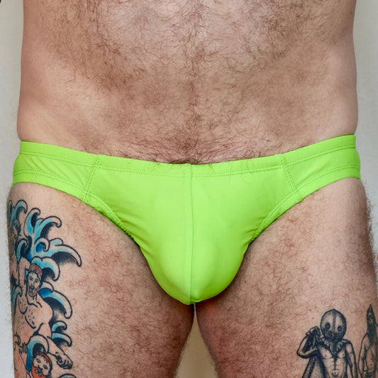 Person wearing bright green swim brief with tattoos visible on the legs.