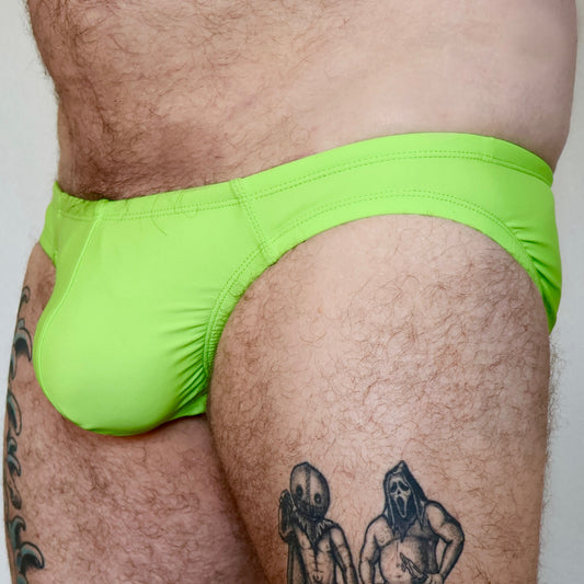Person wearing bright green swim briefs with tattoos visible on the legs.