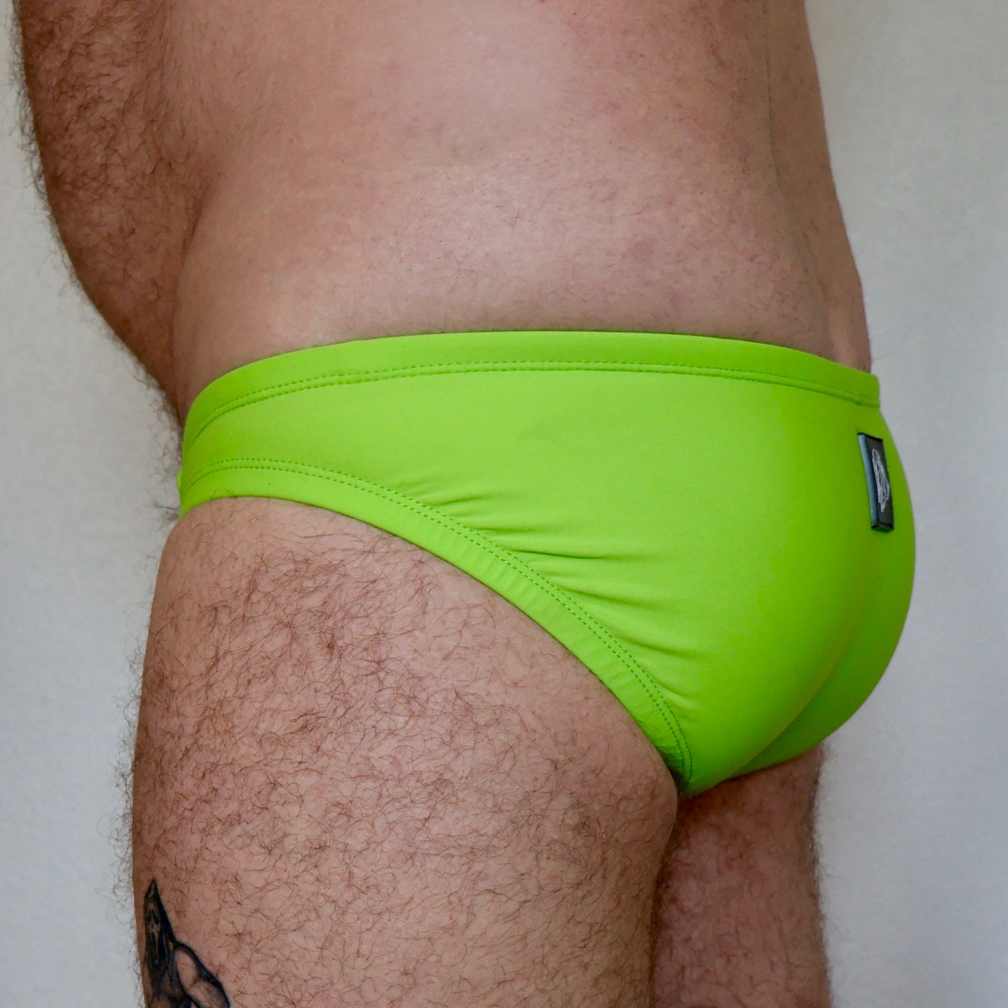 Person wearing bright green swim briefs on a plain background