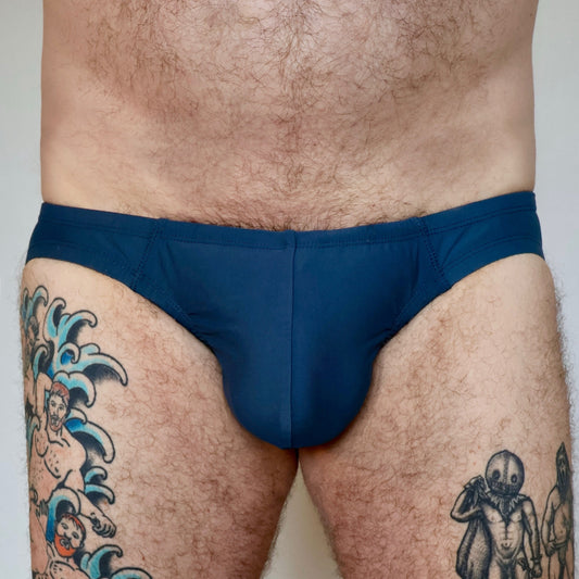 Person wearing a blue swimsuit with tattoos on legs against a plain background