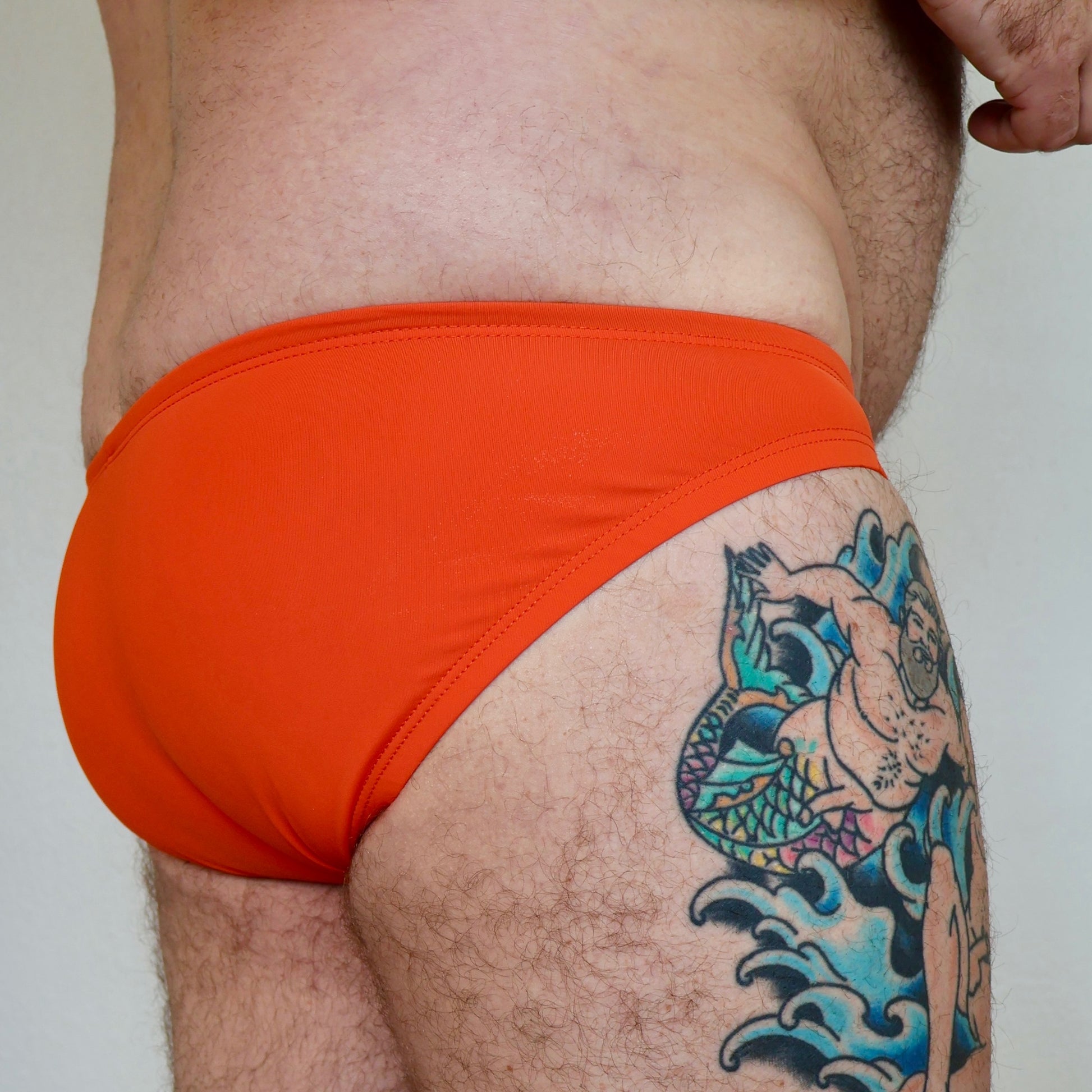 Person wearing bright orange swim briefs with a tattoo on their leg.
