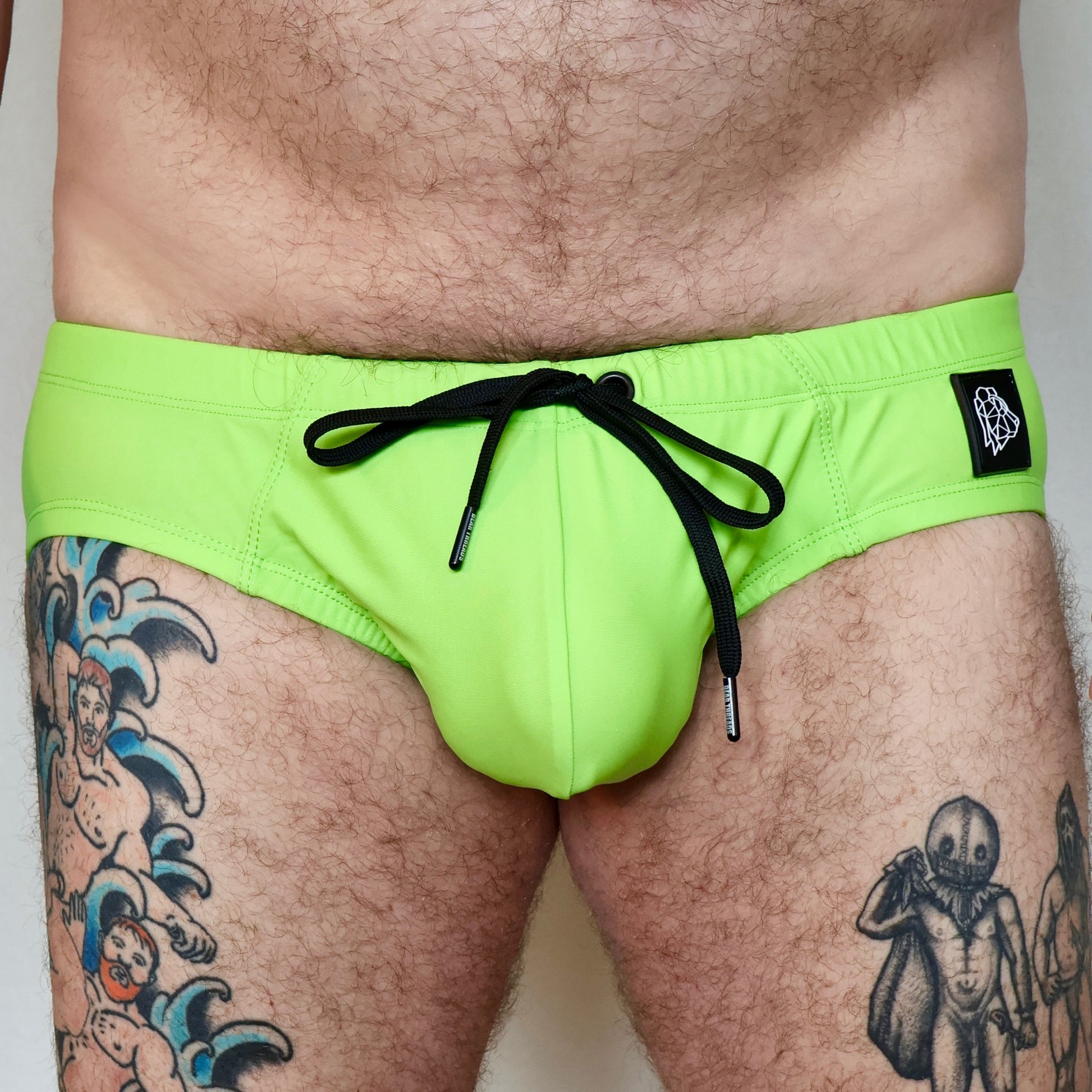 Person wearing bright green swim shorts with a black drawstring on a plain background