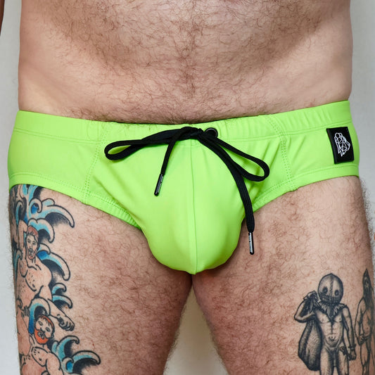 Person wearing bright green swim shorts with a black drawstring on a plain background
