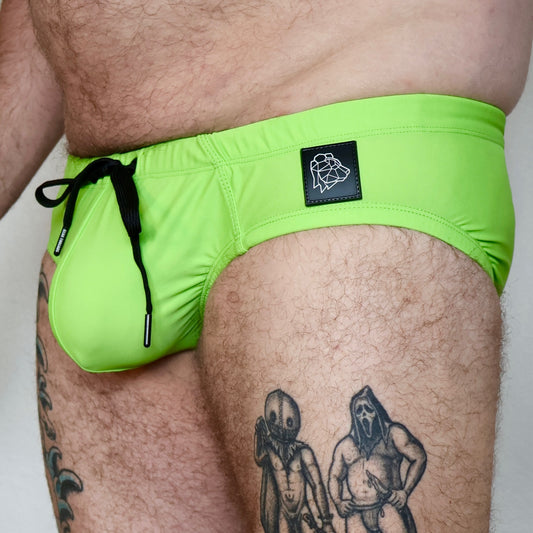Person wearing bright green swim shorts with a visible brand logo on a plain background