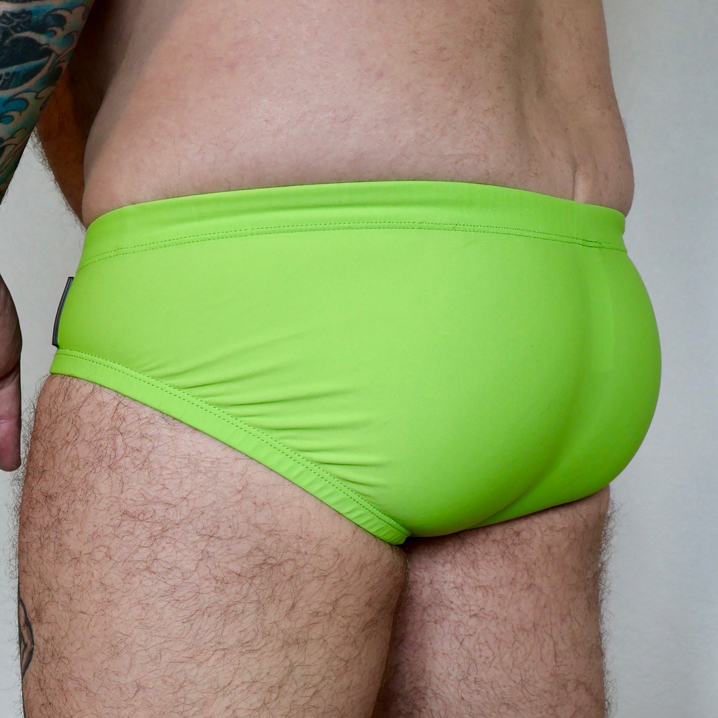 Person wearing bright green swim briefs against a neutral background