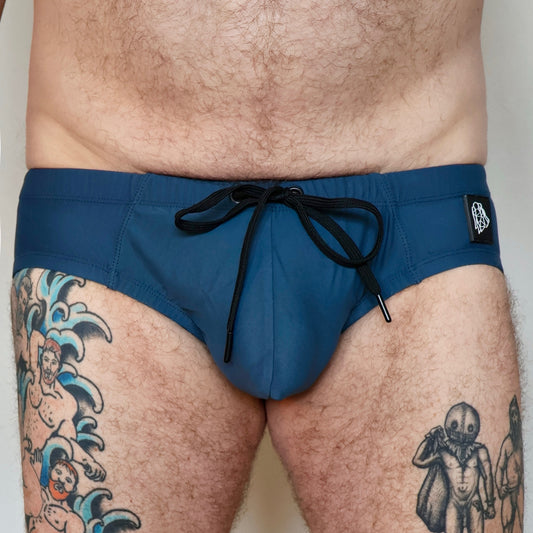 Person wearing blue swim shorts with a tattooed leg on a plain background