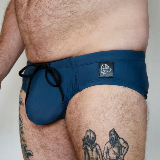 Person wearing blue swim shorts with a brand logo on a plain background