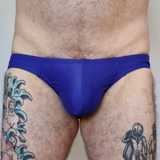 Person wearing a blue men's underwear with tattoos visible on the legs.