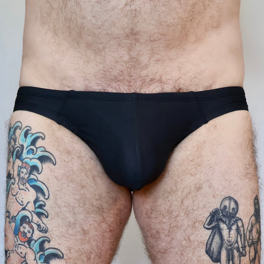 Person wearing black swim briefs with tattoos on arms and legs.