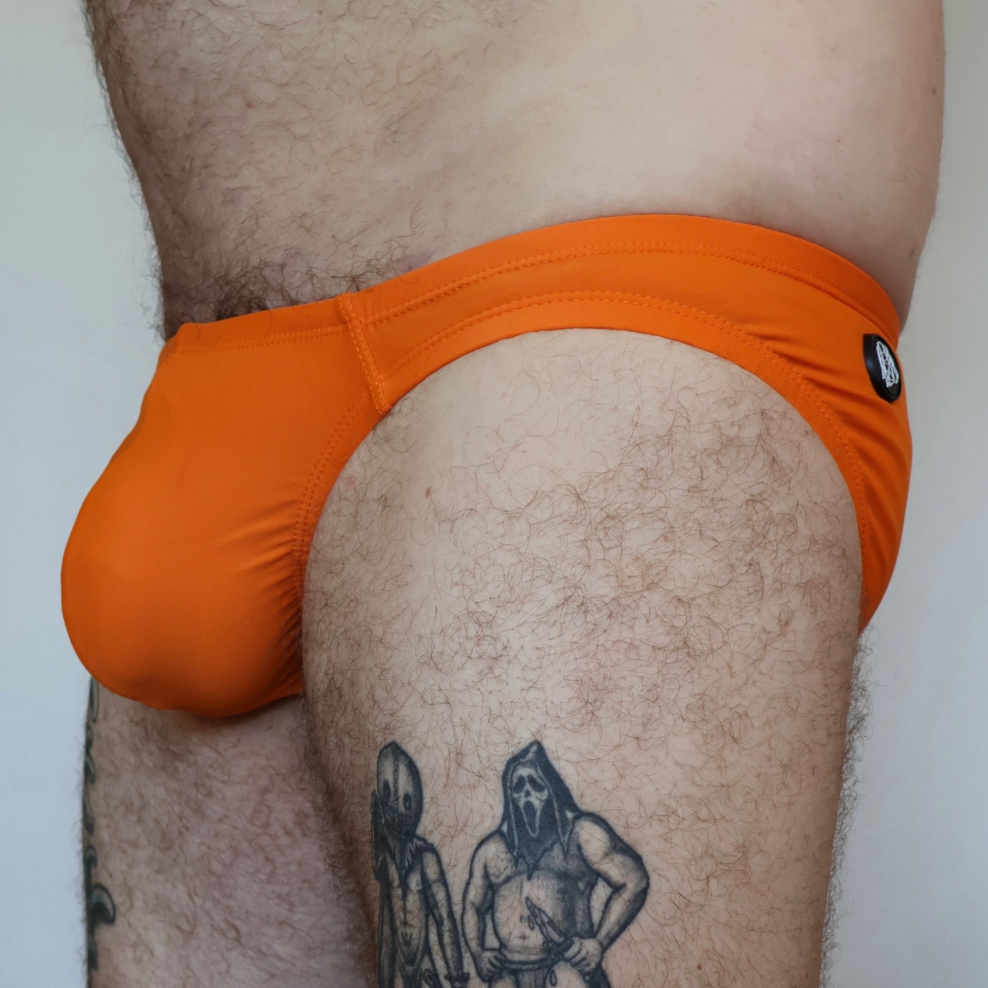 Person wearing orange swim briefs with a tattoo on their leg.