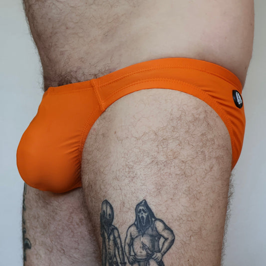 Person wearing orange swim briefs with a tattoo on their leg.