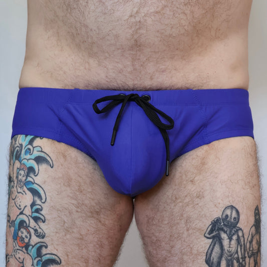 Blue swim brief with black drawstring on a person with tattoos.
