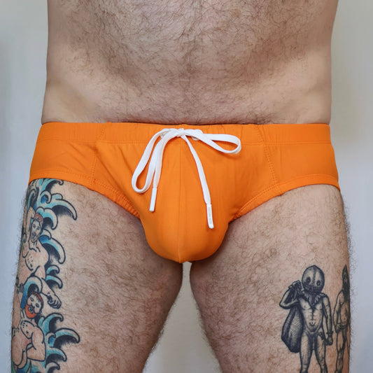 Person wearing bright orange swim trunks with a white drawstring on a plain background