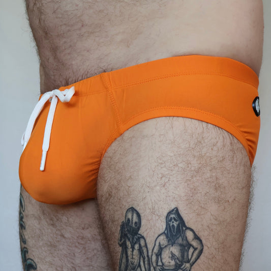 Person wearing orange swim trunks with a white drawstring, standing against a neutral background.