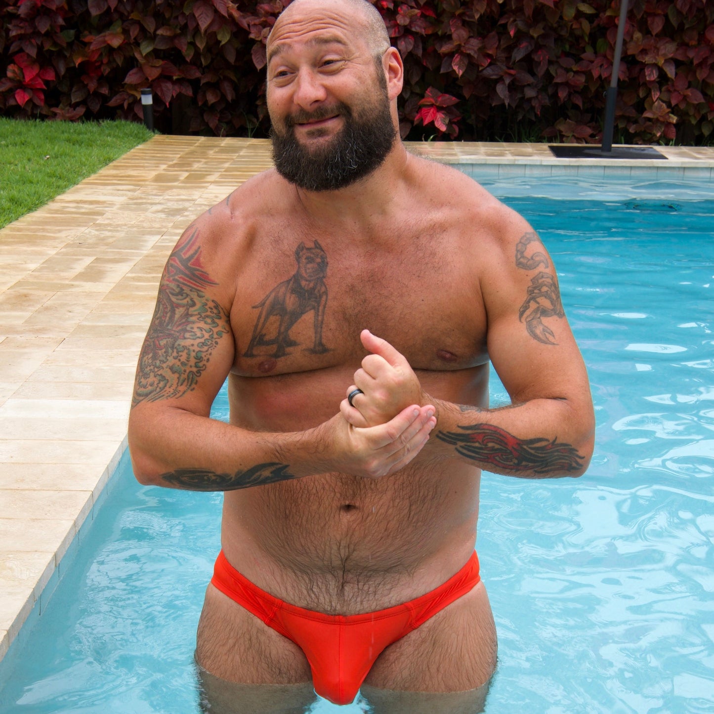 Man in orange swim trunks standing in a pool with tattoos visible