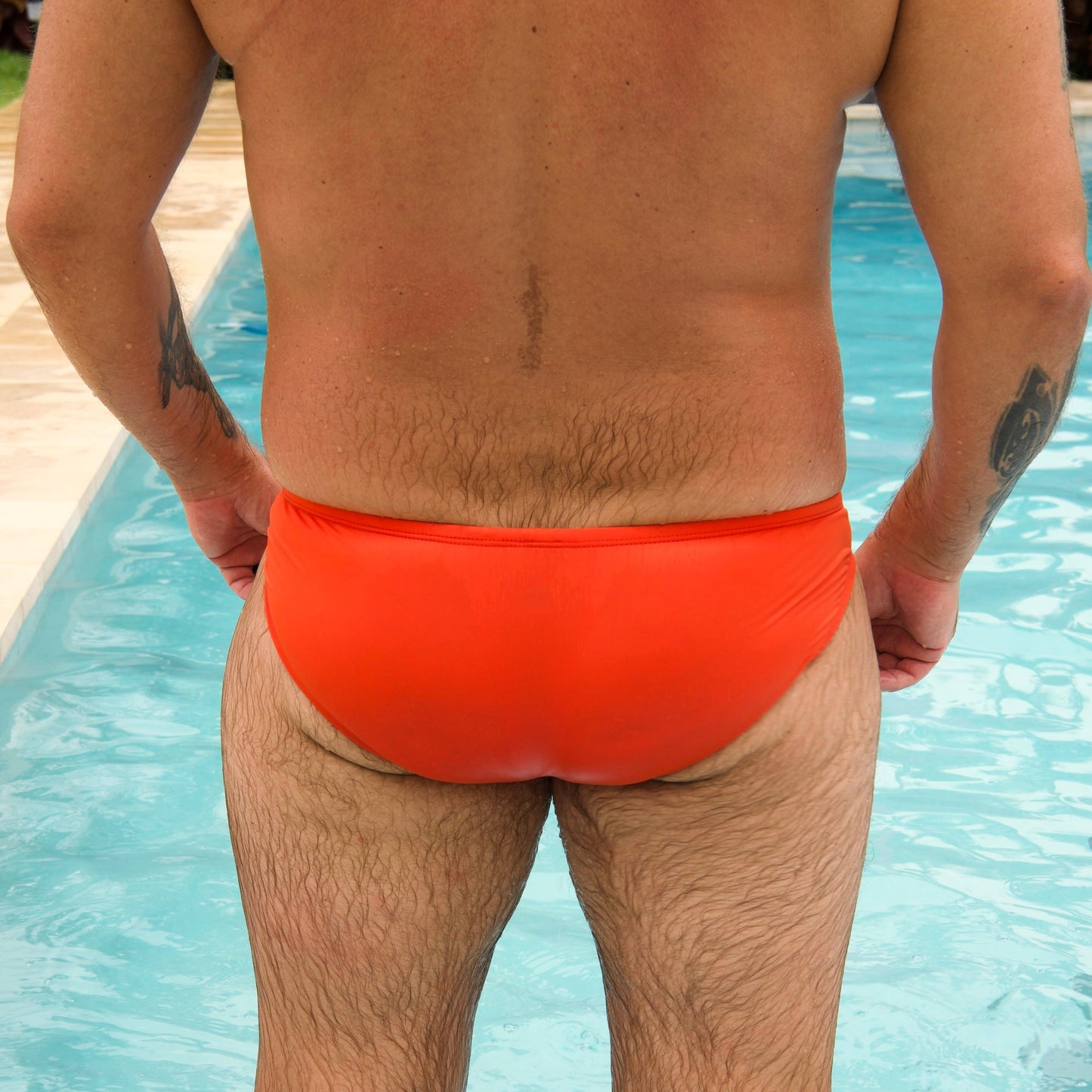 Person wearing bright orange swim briefs standing in a pool.