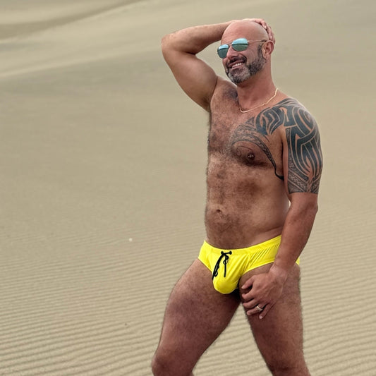 Man in yellow swim shorts standing on a sandy dune