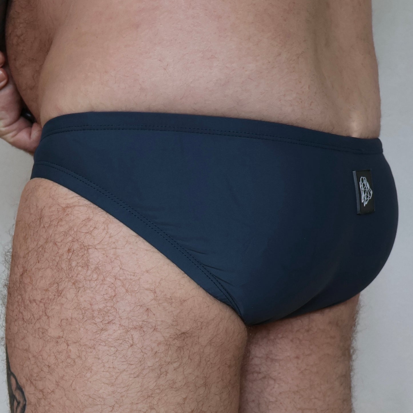 dark grey swim briefs worn by a person against a neutral background